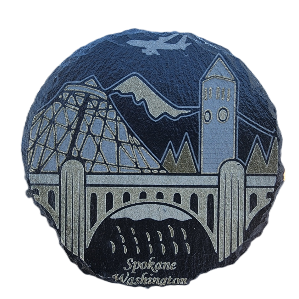 Round decorative item with a design of a bridge, mountains, and buildings, featuring 'Spokane Washington' text.