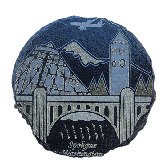Round decorative item with a design of a bridge, mountains, and buildings, featuring 'Spokane Washington' text.